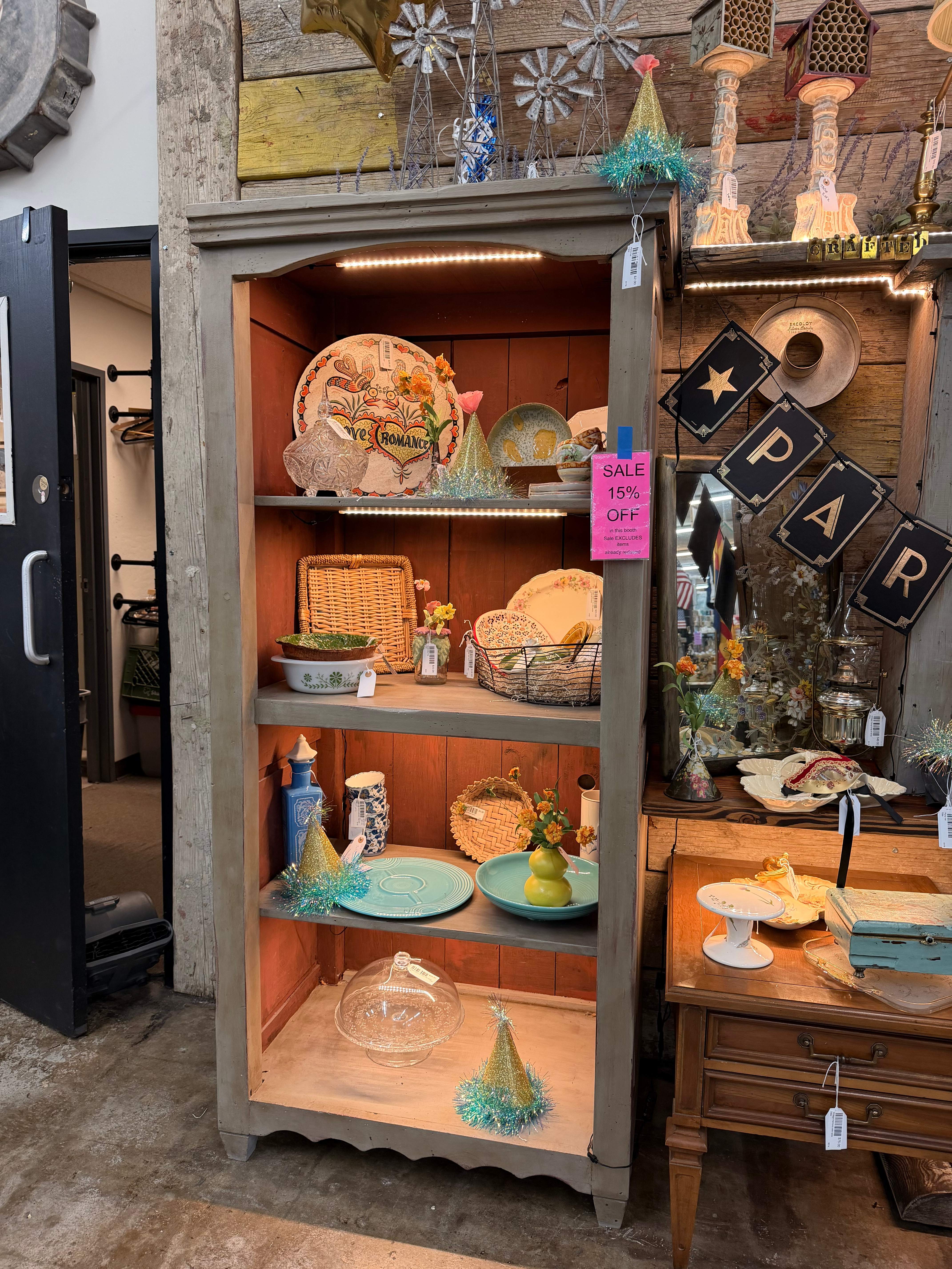 A tall gray hutch styled with vintage plates, woven baskets, teal plates, and glittery party hats